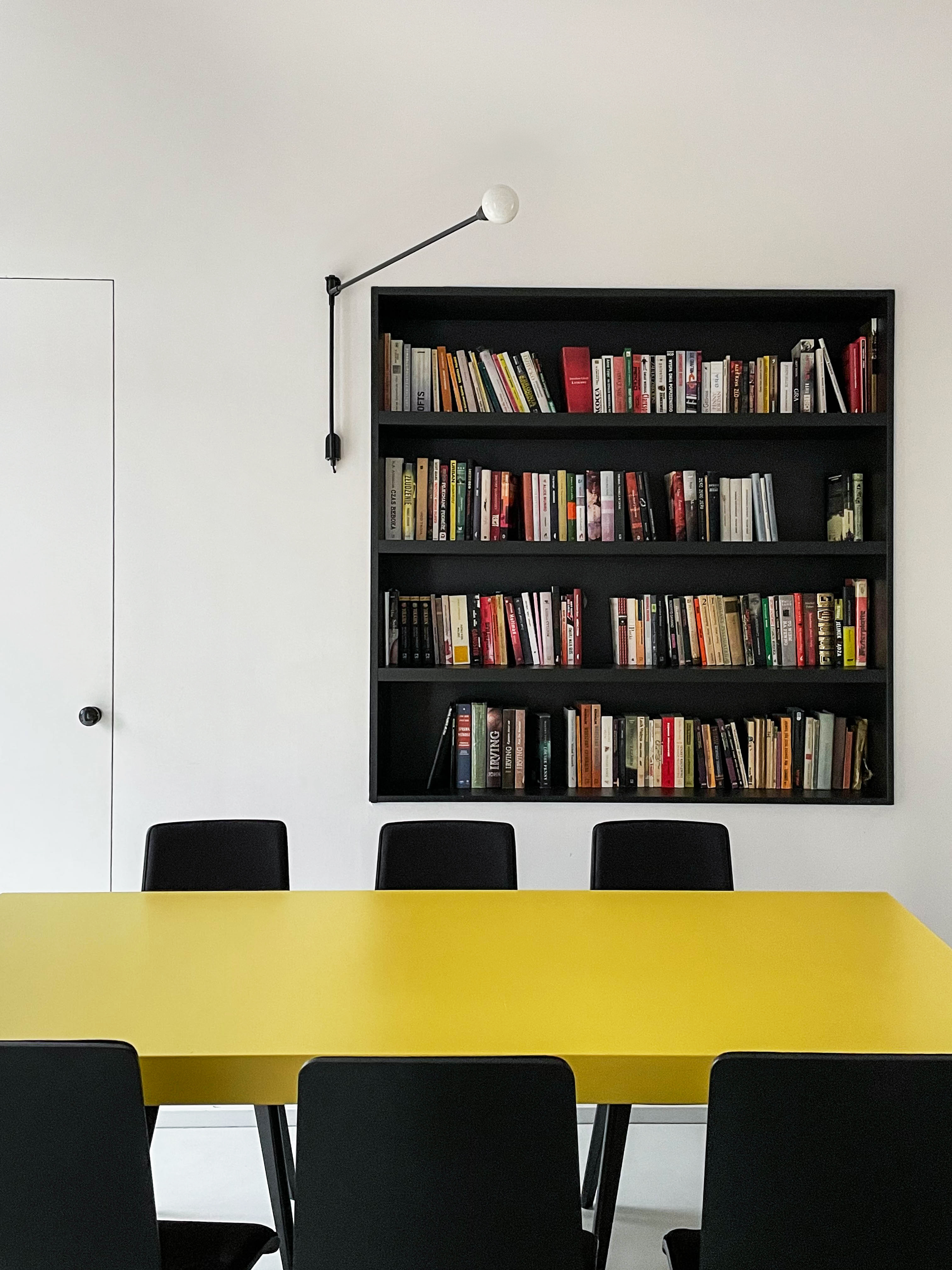 Projekt wnętrza mieszkania w starym spichlerzu - żółty, kubistyczny stół, domowa biblioteczka w czarnym, wpuszczonym w ścianę regale oraz minimalistyczna, liniowa lampa